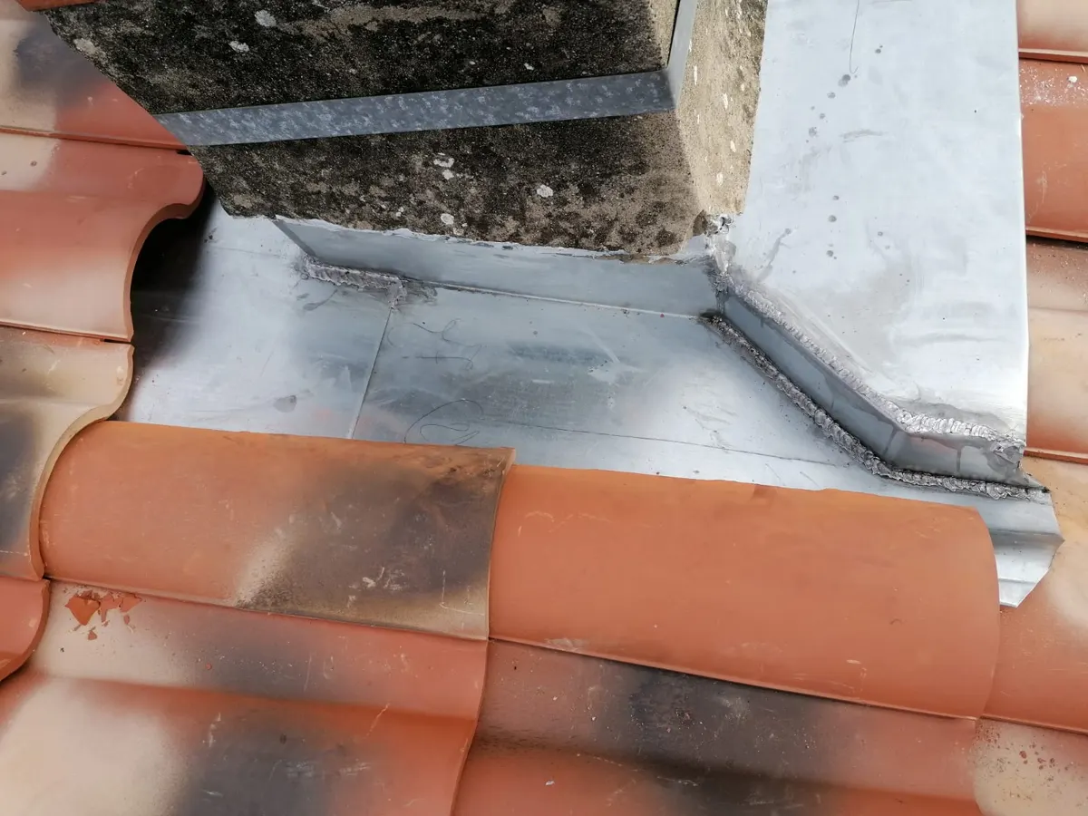 Pièce de zinguerie au pied d’une cheminée sur un toit en tuiles