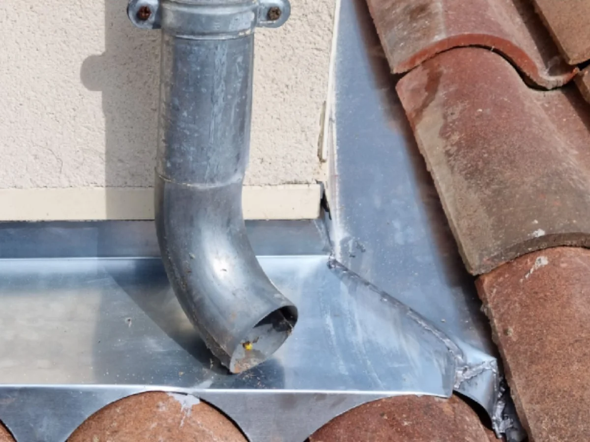 Descente de zinc et raccord de toiture après travaux, avec une vue élargie des tuiles autour